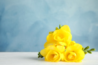 Photo of Beautiful fresh freesia flowers on table against color background. Space for text