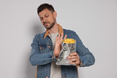 Photo of Handsome man refusing to eat potato chips on light grey background