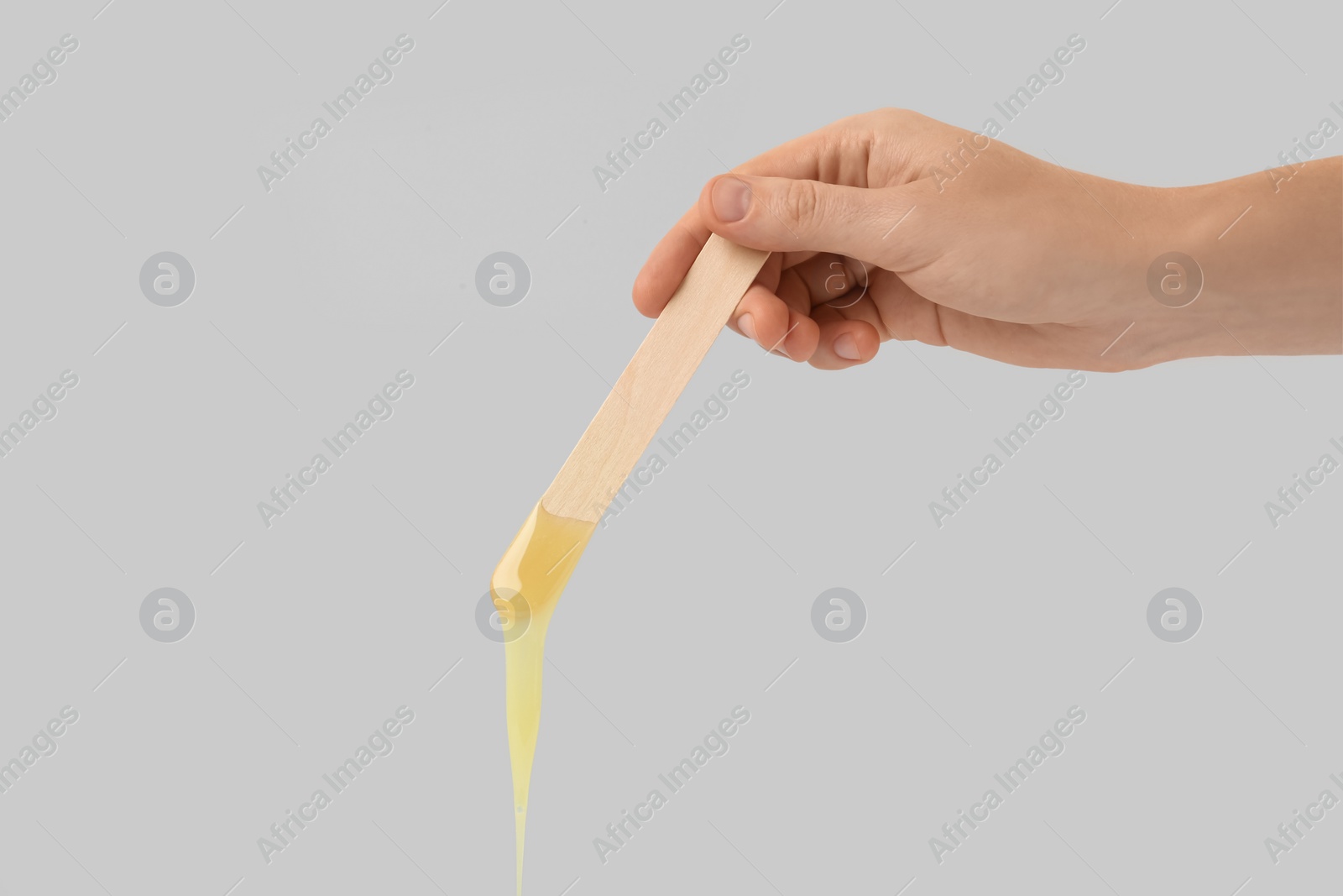 Photo of Woman holding spatula with hot depilatory wax on light  background, closeup