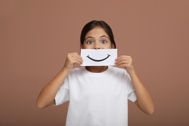 Photo of Little girl holding sheet of paper with smile on pale pink background