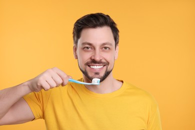 Photo of Happy man holding plastic toothbrush on yellow background. Mouth hygiene