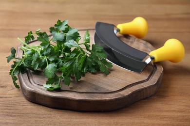 Cutting board with parsley and mezzaluna knife on wooden table