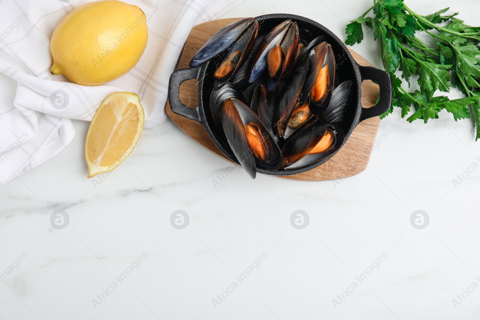 Photo of Pan of cooked mussels with parsley and lemon on white marble table, flat lay. Space for text