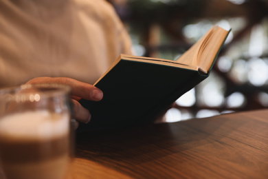 Man reading book at wooden table, closeup