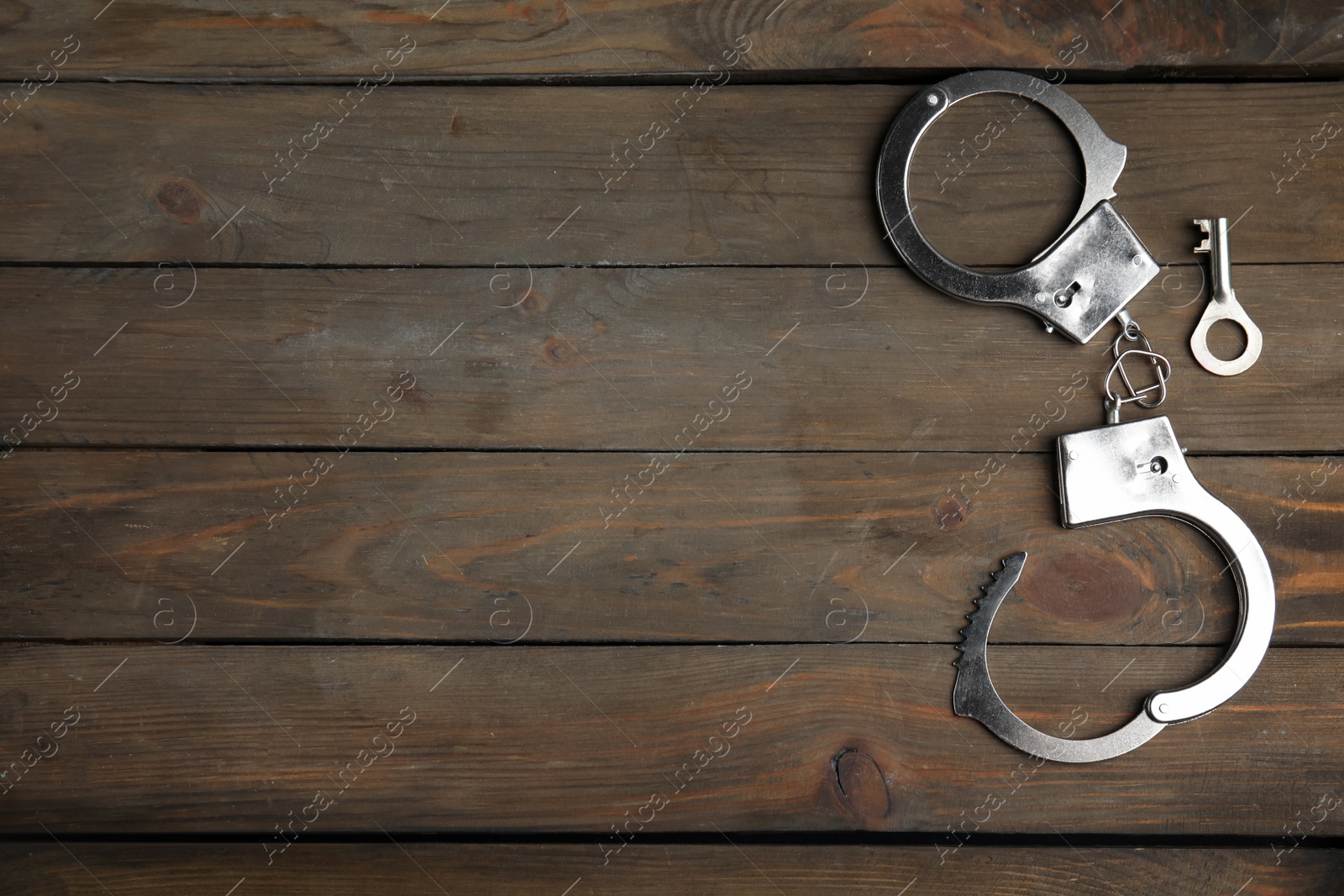 Photo of Classic chain handcuffs with key on wooden table, flat lay. Space for text