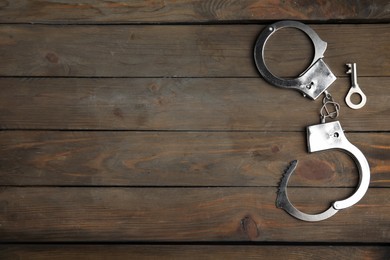 Photo of Classic chain handcuffs with key on wooden table, flat lay. Space for text