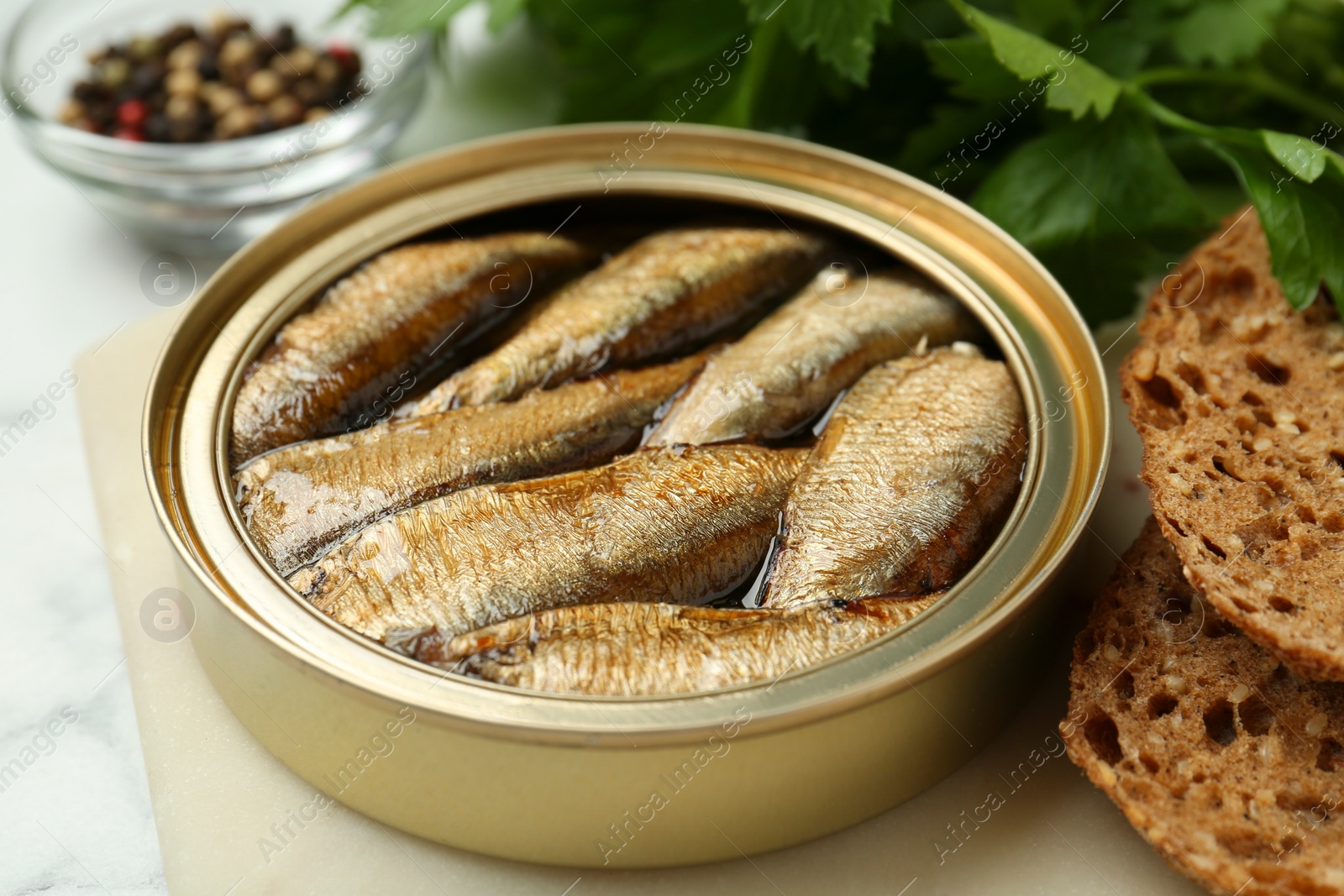 Photo of Tin can with tasty sprats served on board, closeup