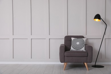 Photo of Grey armchair and lamp near empty molding wall indoors, space for text