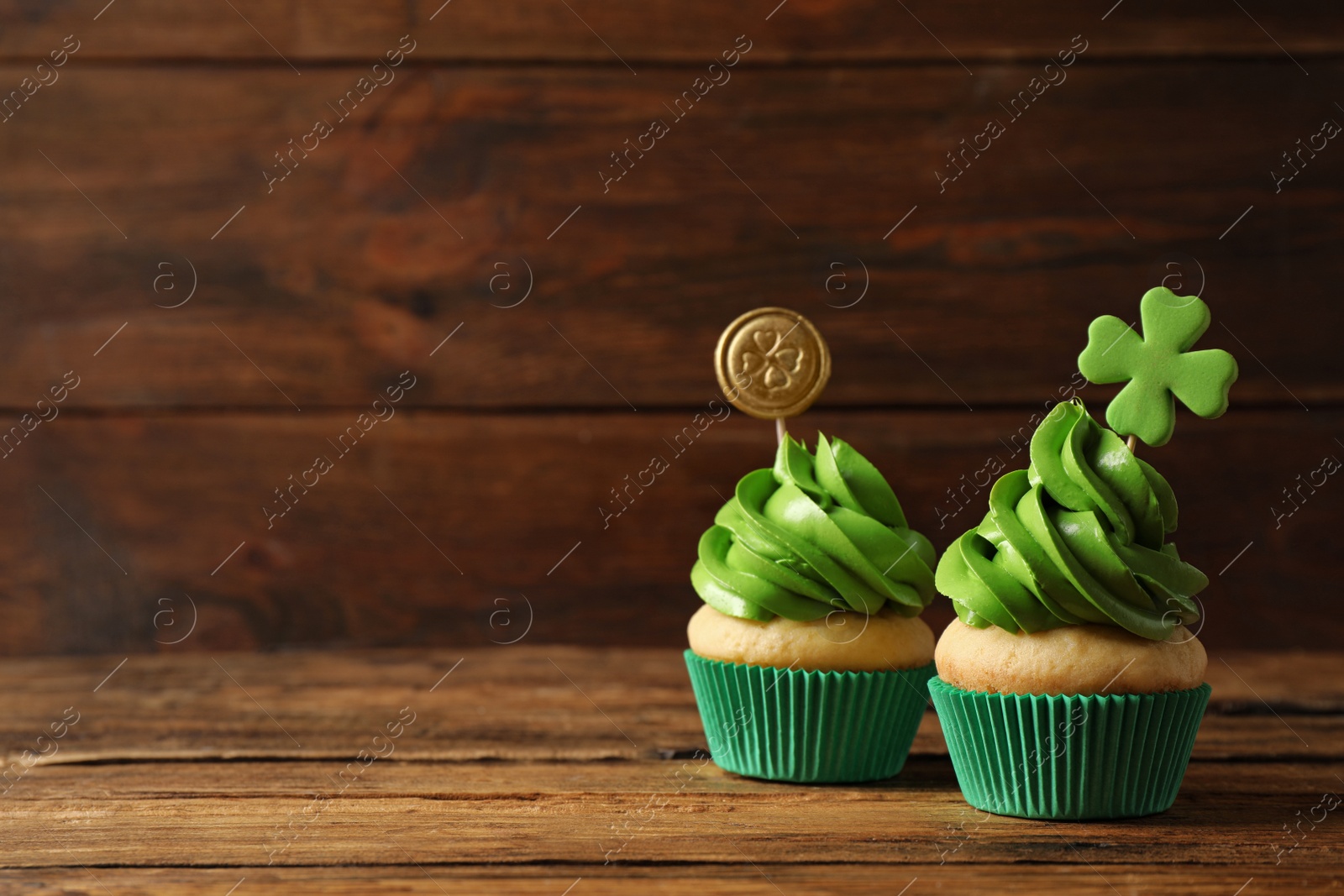 Photo of Delicious decorated cupcakes on wooden table, space for text. St. Patrick's Day celebration