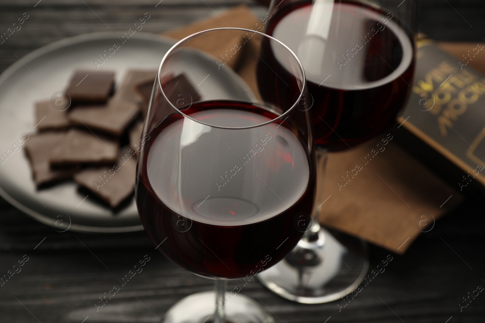 Photo of Tasty red wine and chocolate on black wooden table, closeup