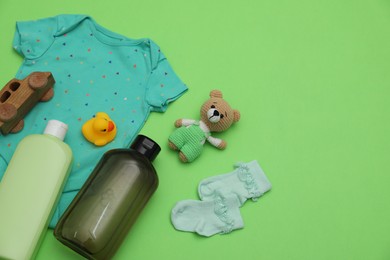 Bottles of laundry detergents, baby clothes and toys on light green background, flat lay. Space for text