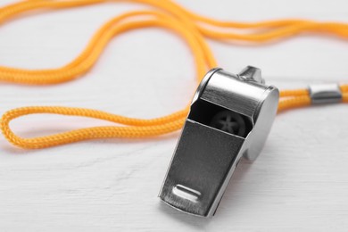One metal whistle with cord on white wooden table, closeup