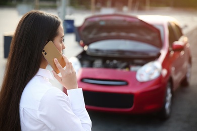 Stressed woman talking on phone near broken car outdoors