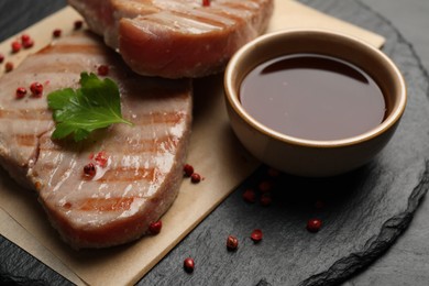 Photo of Delicious tuna steaks with sauce, parsley and spices on table, closeup