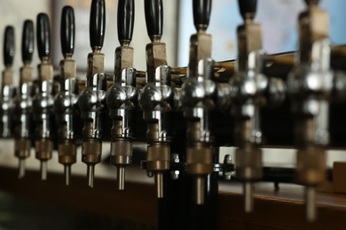 Photo of New modern beer taps in pub, closeup. Professional bar equipment