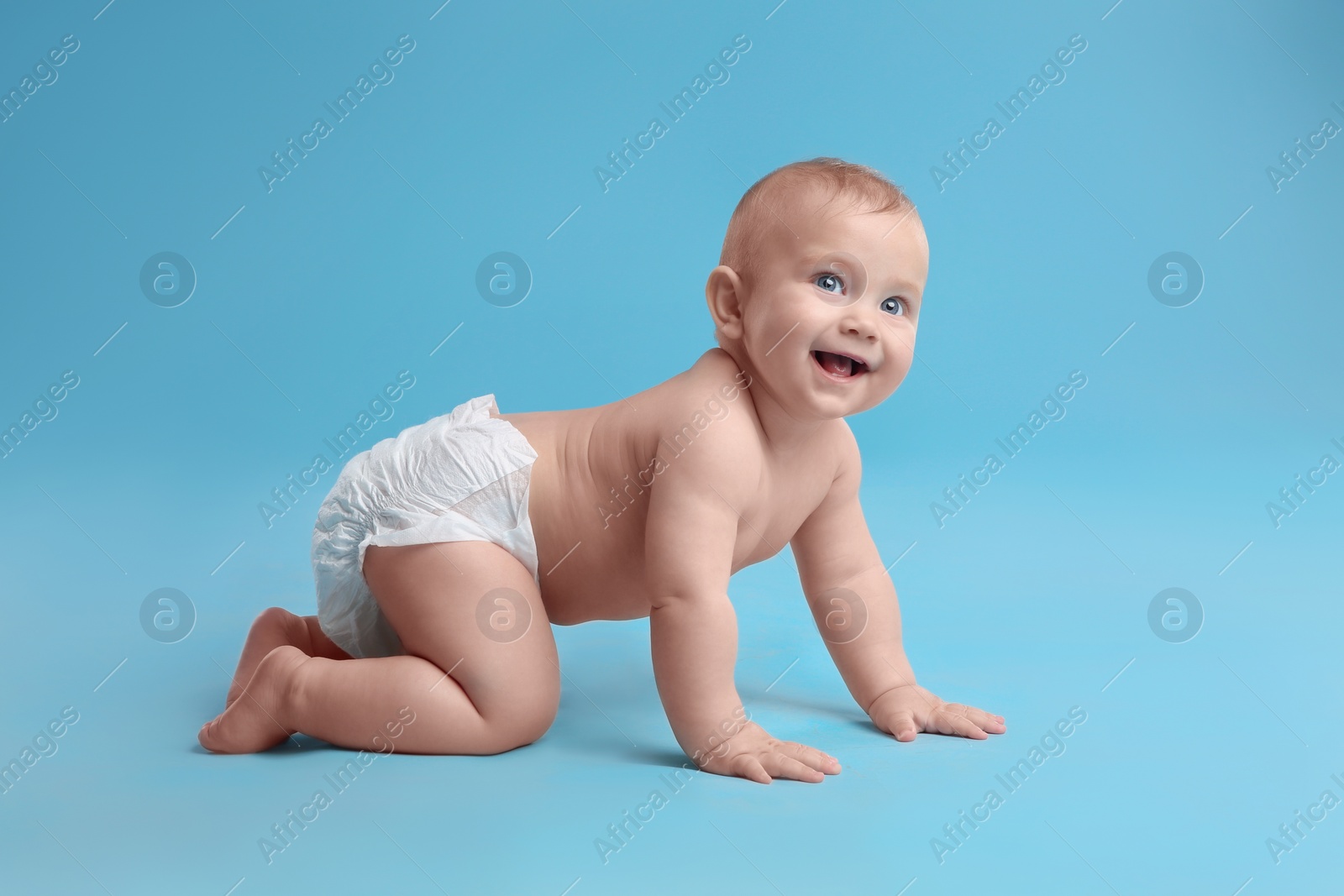 Photo of Cute baby in dry soft diaper crawling on light blue background