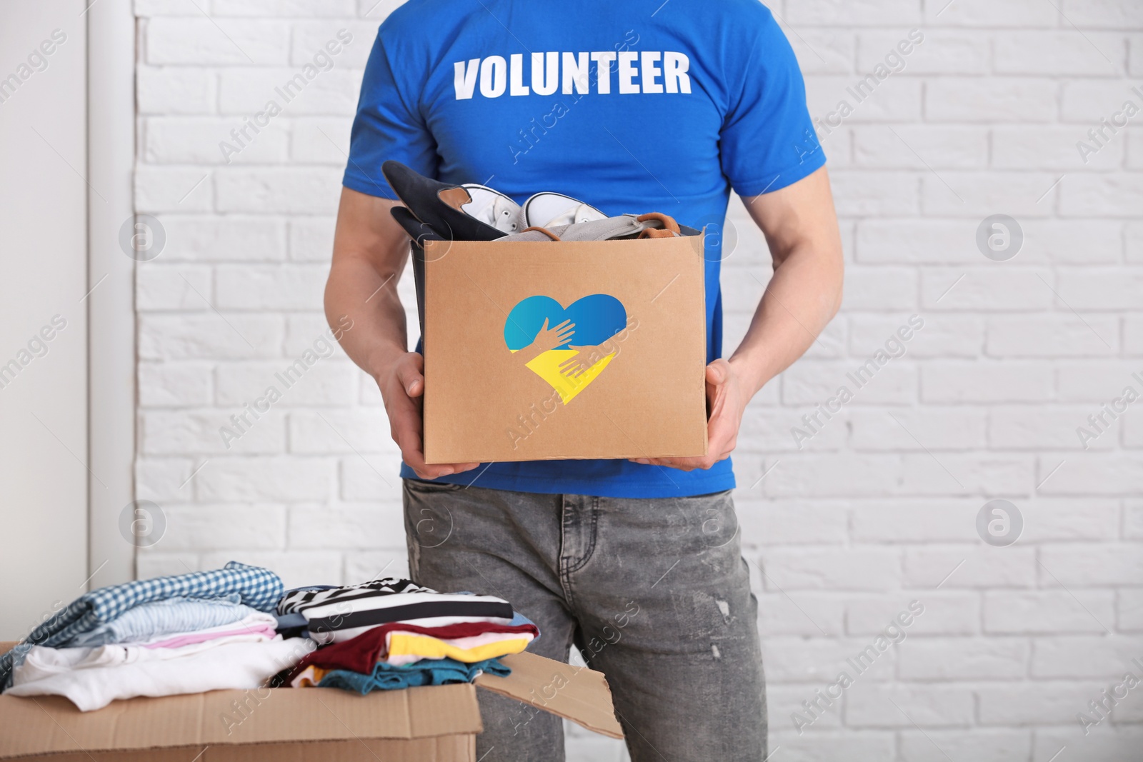 Image of Humanitarian aid for Ukrainian refugees. Volunteer holding donation box with shoes indoors