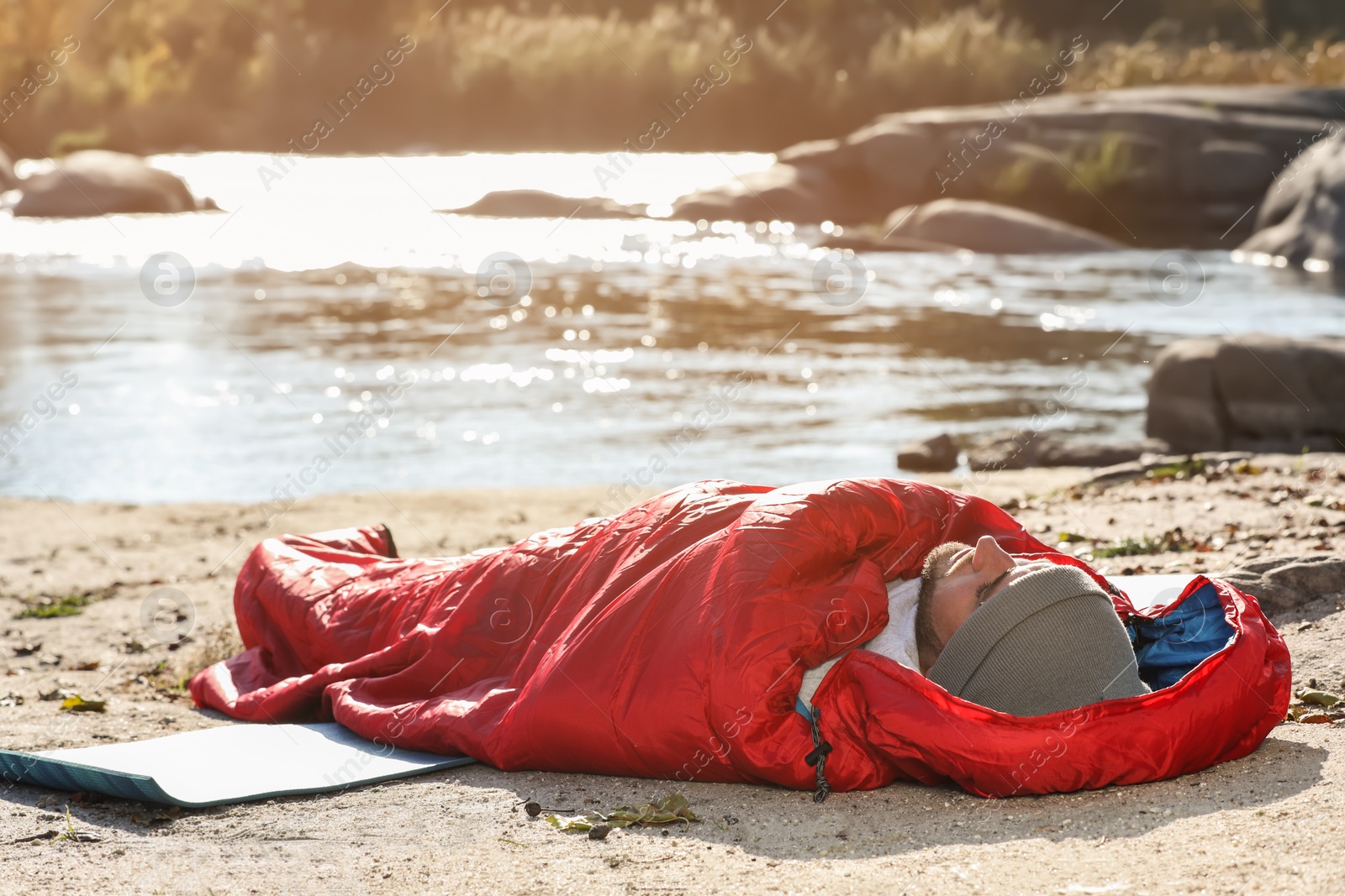 Photo of Man in sleeping bag on wild beach. Camping equipment