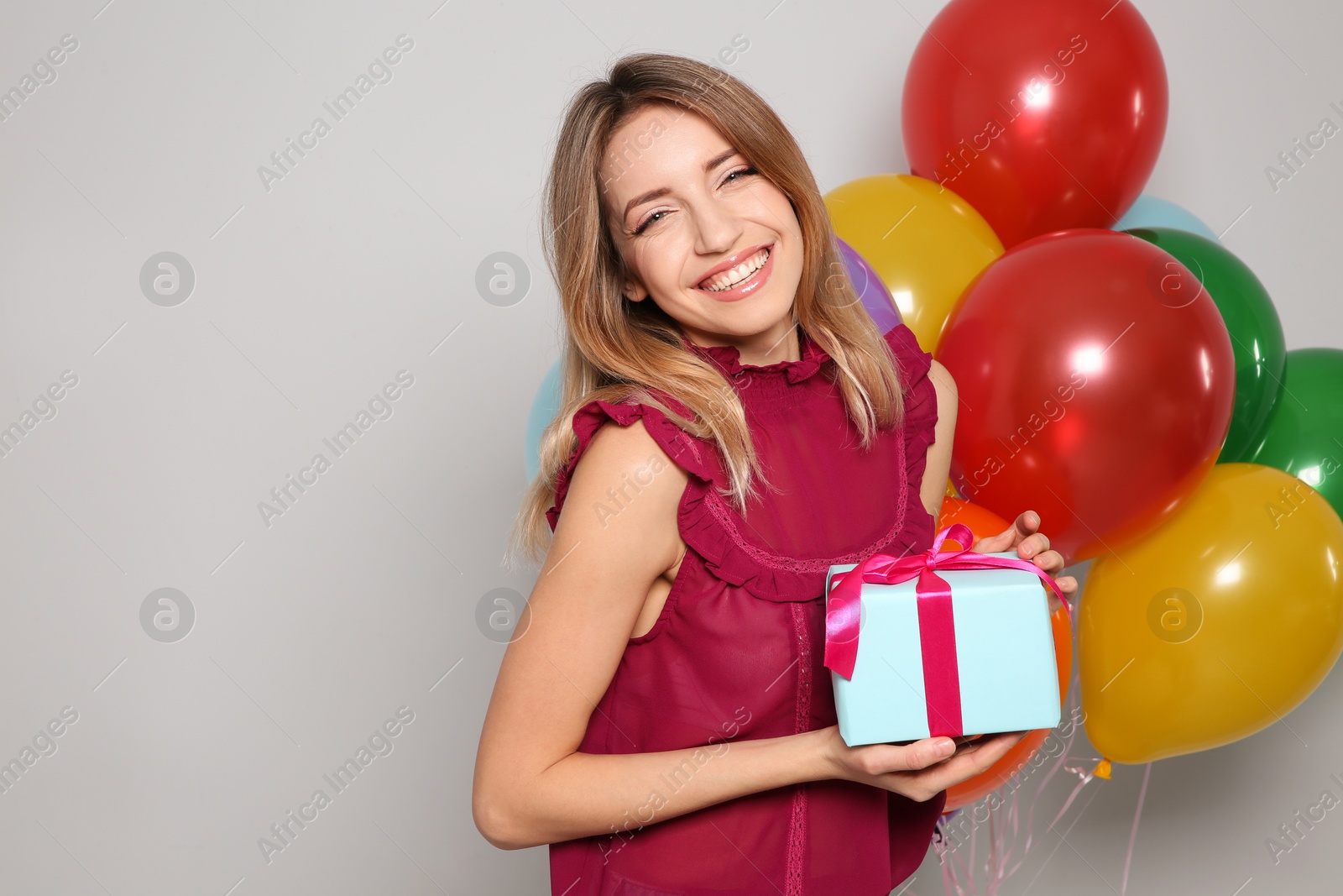 Photo of Portrait of beautiful smiling girl with gift box and air balloons on light background. International Women's Day