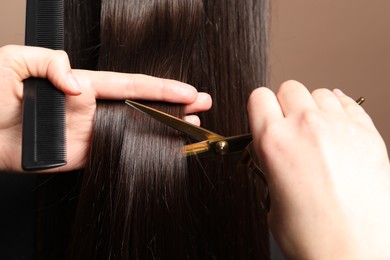 Photo of Hairdresser cutting client's hair with scissors on light brown background, closeup