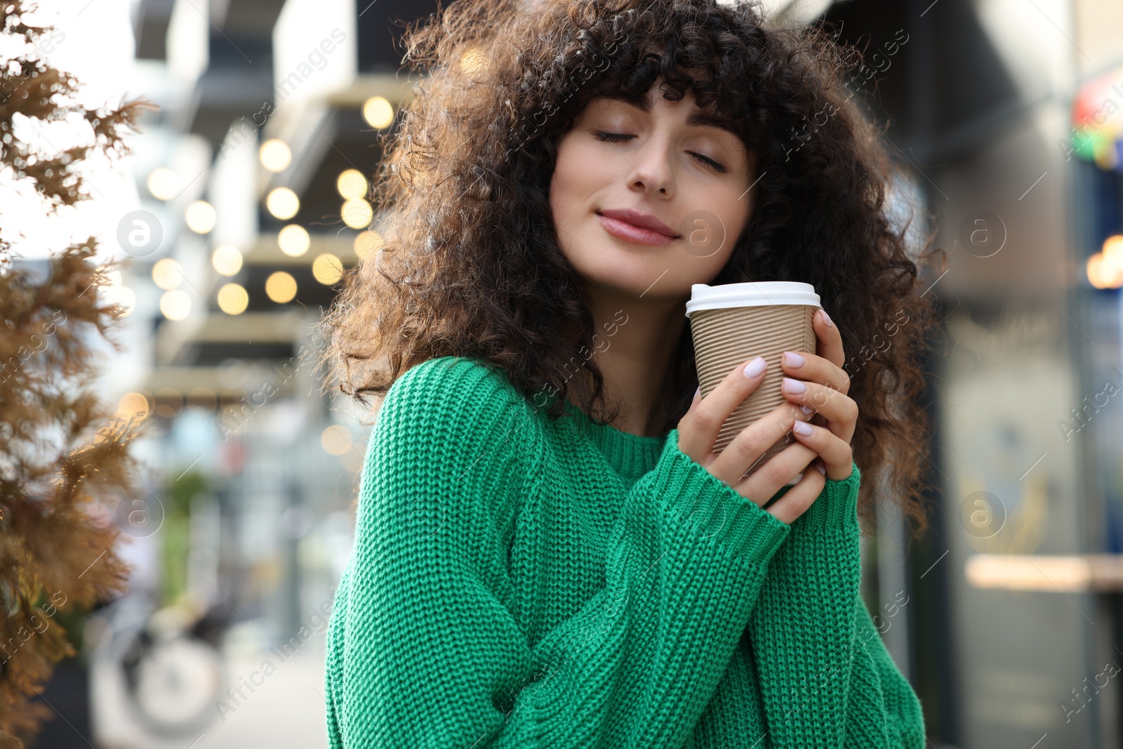 Photo of Young woman in stylish green sweater with cup of coffee outdoors