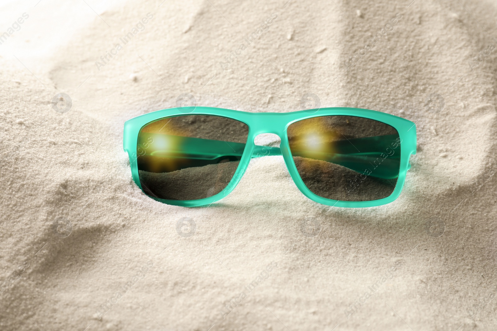 Photo of Stylish sunglasses on white sand. Fashionable accessory