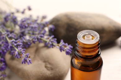 Photo of Bottle of essential oil and lavender flowers on white table, closeup. Space for text