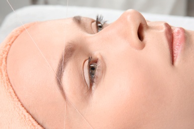 Photo of Young woman having eyebrow correction procedure in beauty salon, closeup