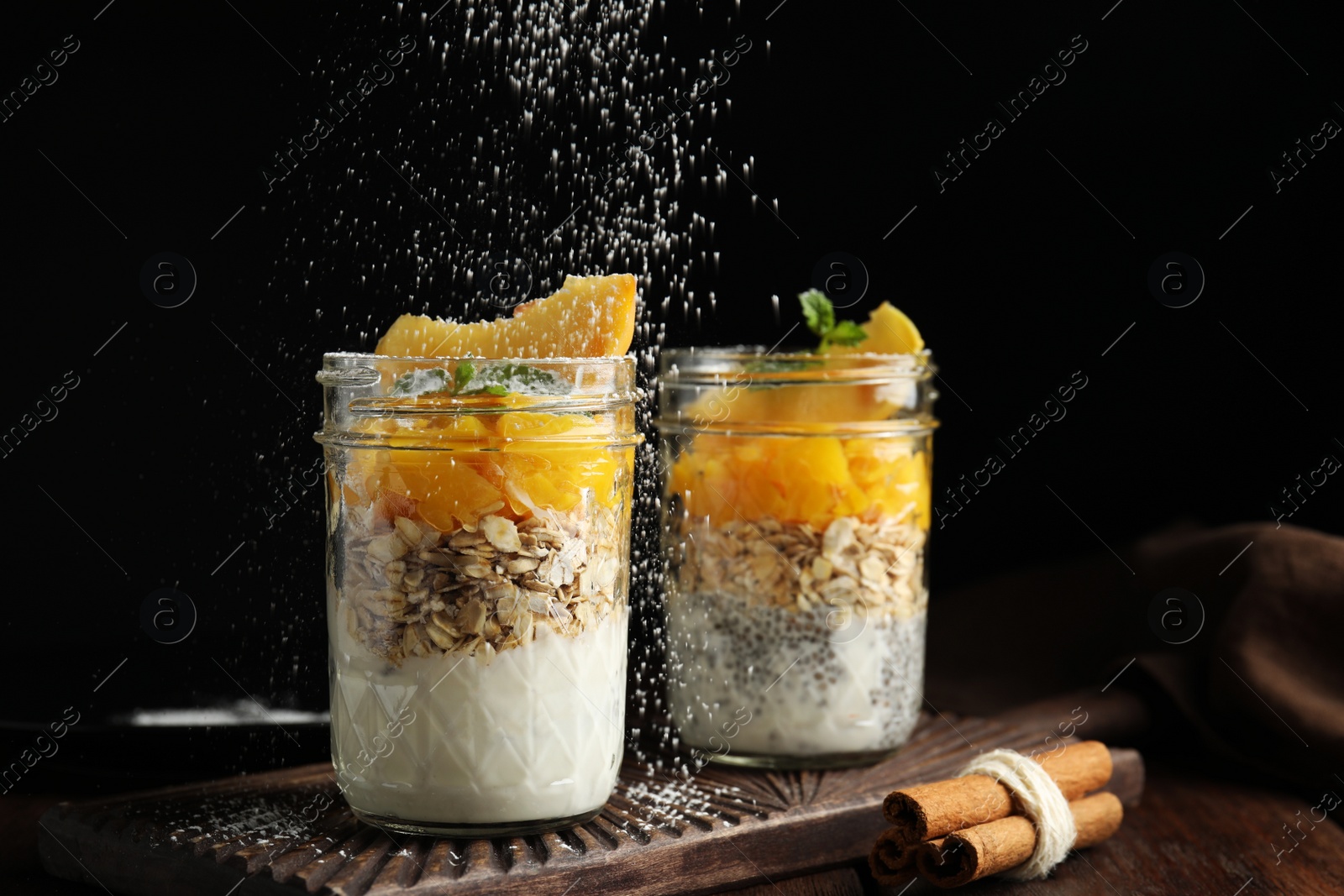 Photo of Powdering tasty peach dessert with icing sugar on black background