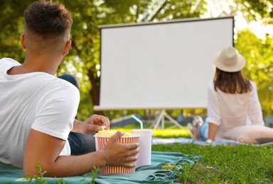 Young man with popcorn and drink watching movie in open air cinema. Space for text