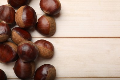 Photo of Sweet fresh edible chestnuts on light wooden table, top view. Space for text