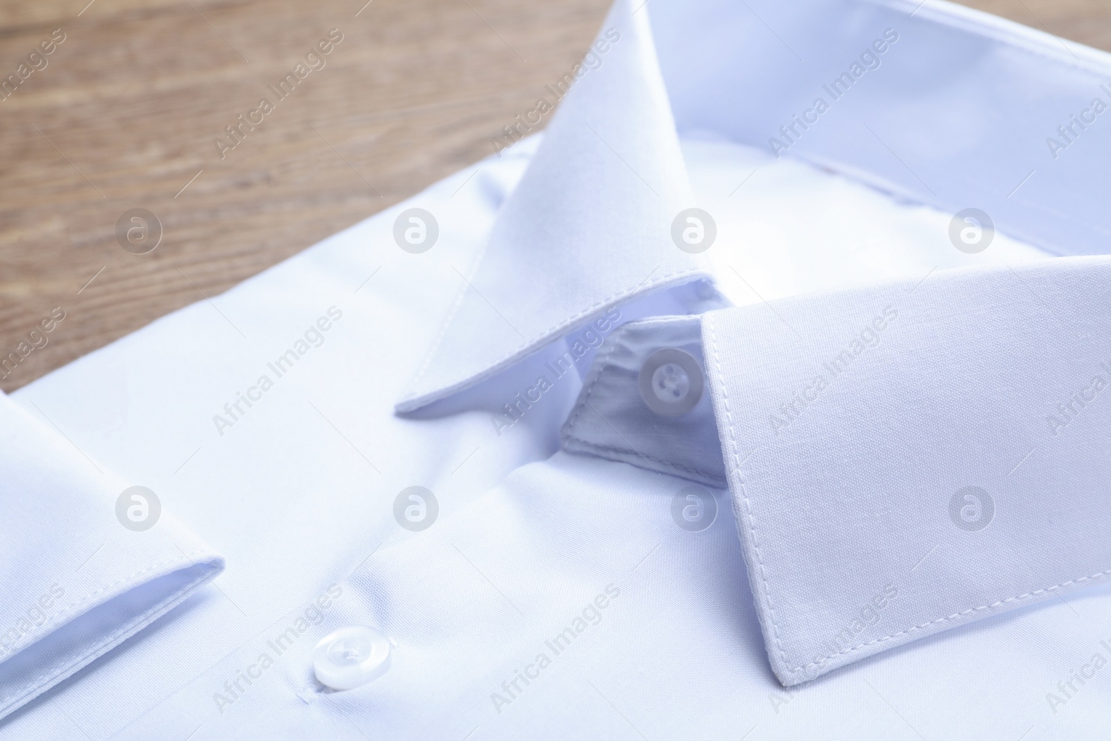 Photo of Stylish white shirt on wooden table, closeup. Dry-cleaning service