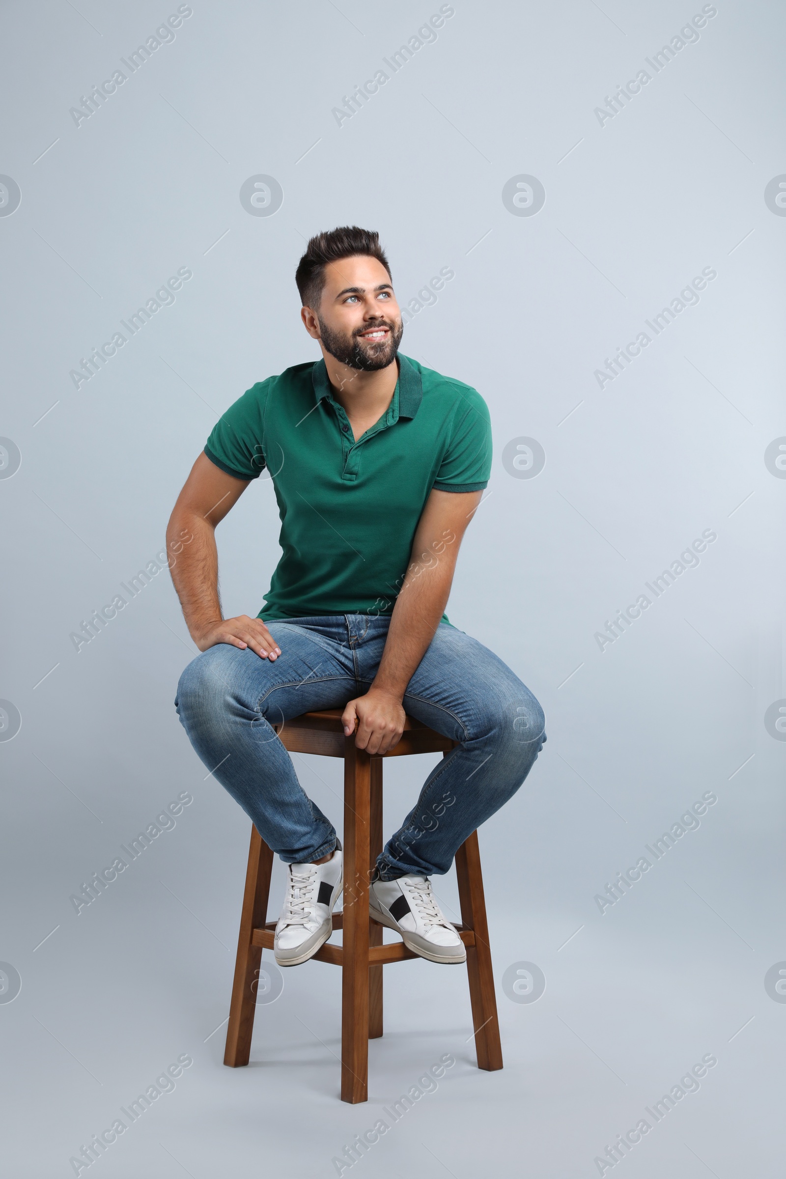 Photo of Handsome young man sitting on stool against light grey background