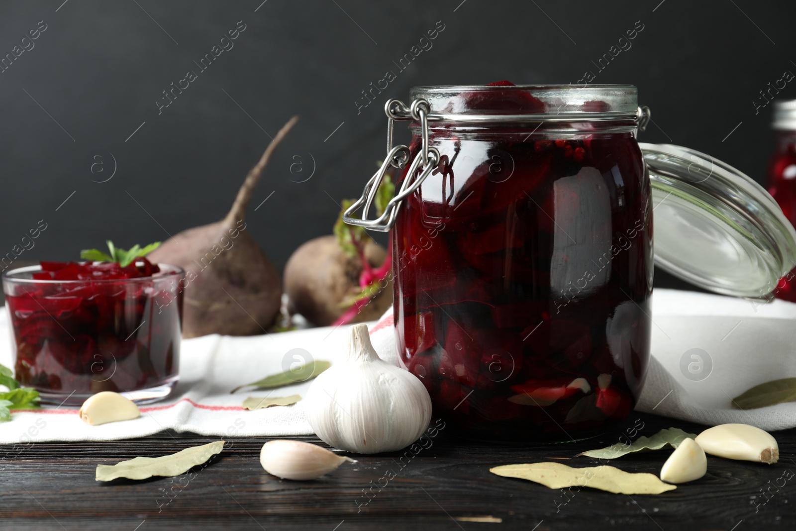 Photo of Pickled beets in glass jar on wooden table against dark background