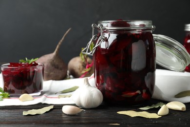 Photo of Pickled beets in glass jar on wooden table against dark background