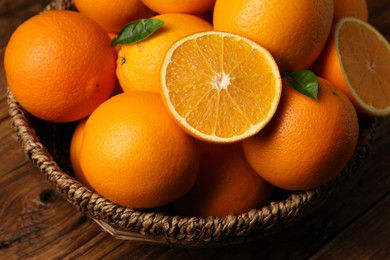 Photo of Many ripe oranges and green leaves on wooden table, closeup