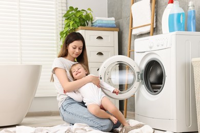 Mother with her daughter having fun while washing baby clothes in bathroom