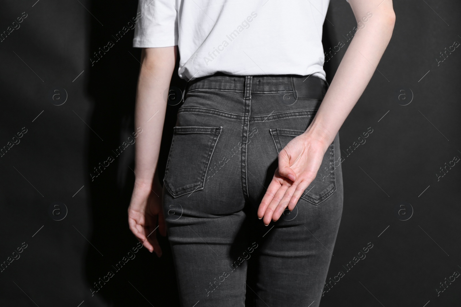 Photo of Woman showing open palm behind her back on black background, back view