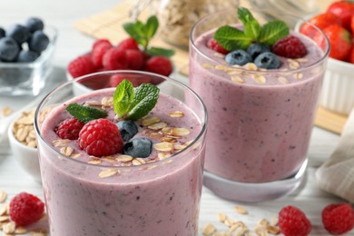 Photo of Tasty smoothie with berries, mint and oatmeal on white table, closeup