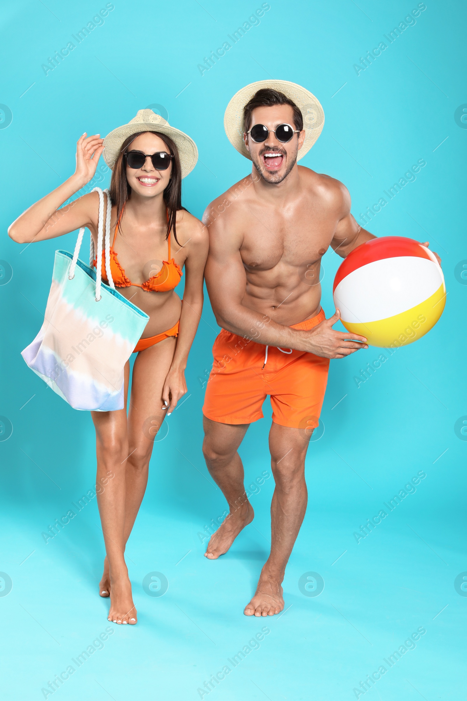 Photo of Young attractive couple in beachwear with ball and bag on blue background