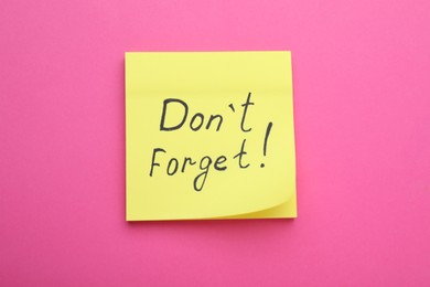 Photo of Paper note with phrase Don't Forget on pink background, top view
