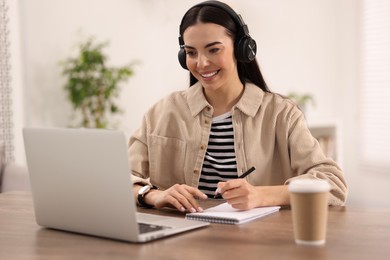 Young woman in headphones watching webinar at table in room