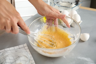 Woman whisking dough for cake at light grey table, closeup
