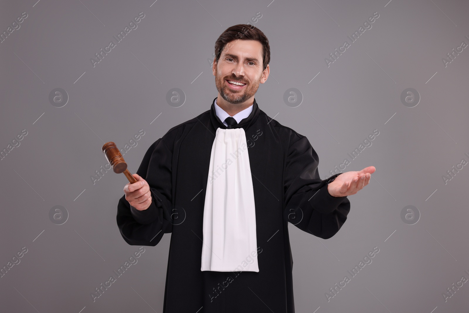 Photo of Happy judge with gavel on grey background