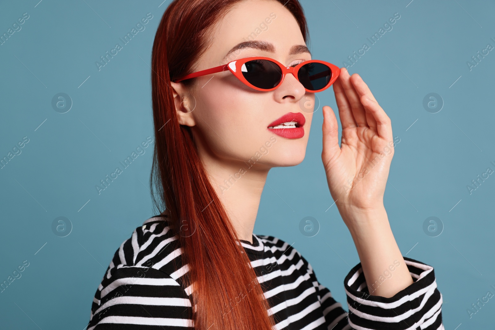 Photo of Stylish woman with red dyed hair and sunglasses on light blue background