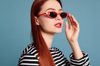Photo of Stylish woman with red dyed hair and sunglasses on light blue background