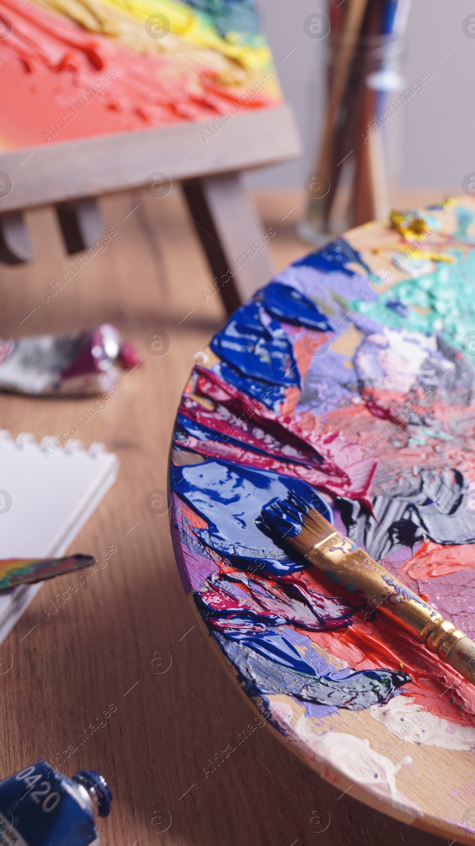 Photo of Applying paint with brush on artist's palette at wooden table, closeup