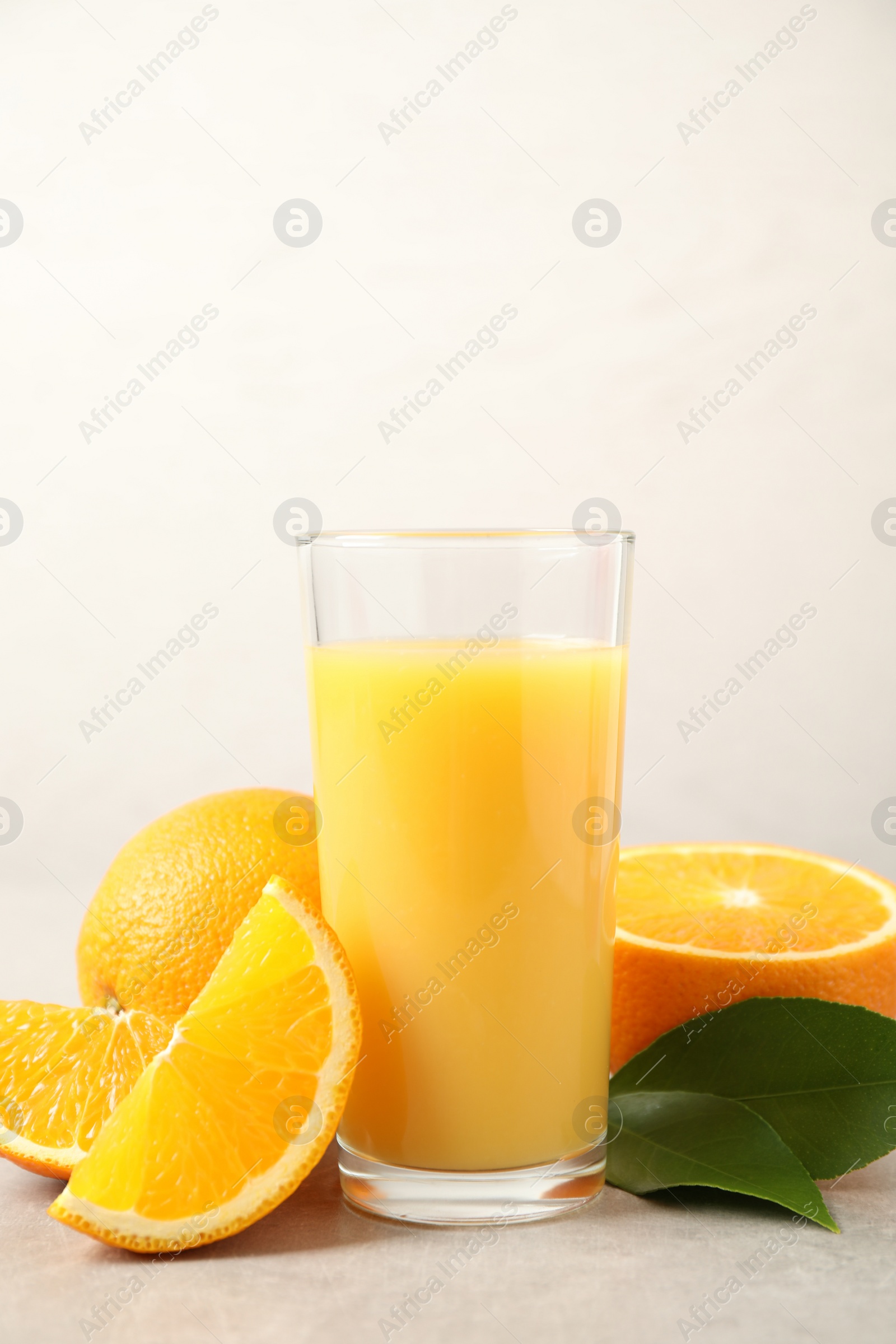 Photo of Tasty orange juice, fresh fruits and green leaves on light table