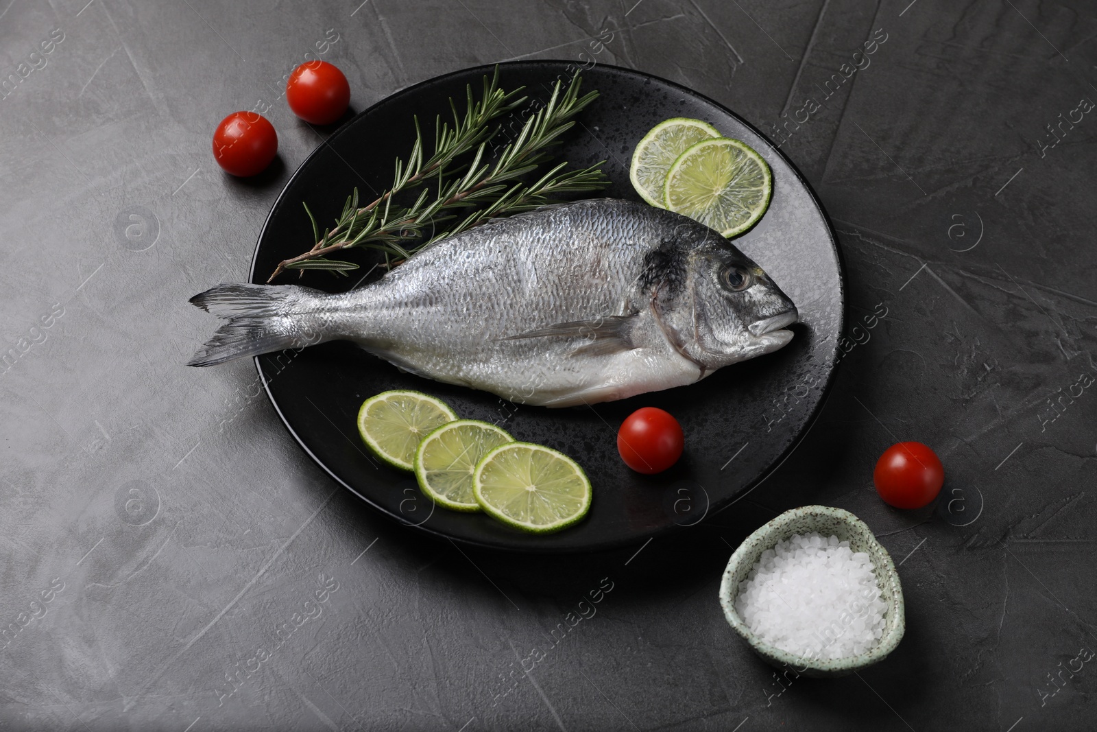 Photo of Fresh dorado fish, lime, tomatoes and rosemary on grey table, above view