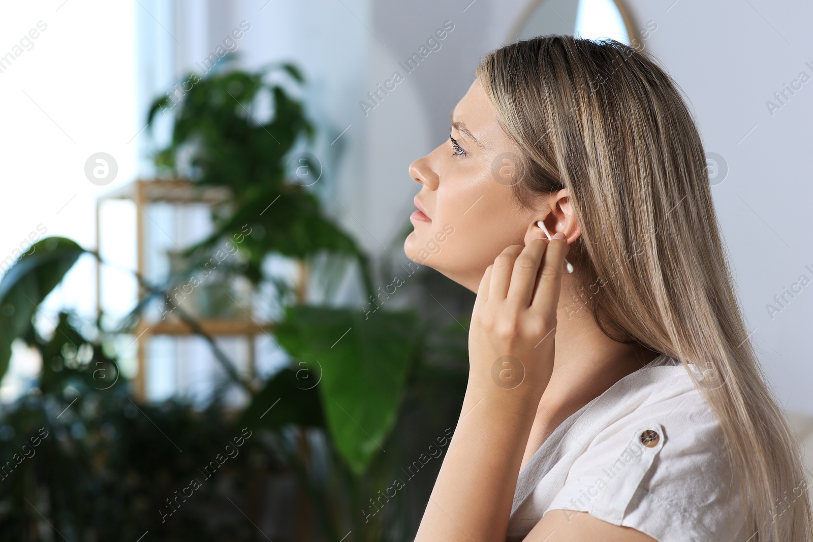 Photo of Young woman cleaning ear with cotton swab at home. Space for text